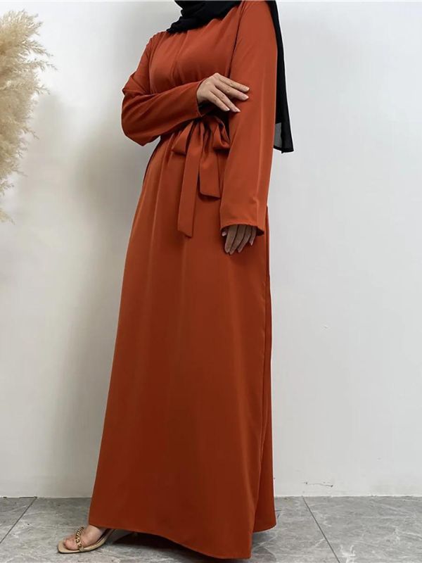 La femme porte une abaya longue de couleur orange vif, vue de face