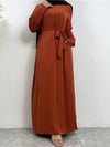 La femme porte une abaya longue de couleur orange vif, vue de face. La robe est ample et descend jusqu&#39;au sol, mettant en valeur la coupe fluide et élégante de l&#39;abaya