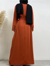 La femme porte une abaya longue de couleur orange vif, vue de dos. La robe est ample et descend jusqu&#39;au sol, offrant une vue complète de la coupe fluide et élégante de l&#39;abaya