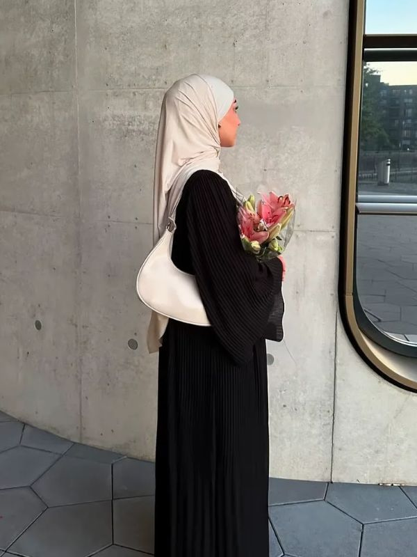 Abaya plissée noire Lys d'Ébène portée de trois quarts, la manche évasée plissée enveloppant un bouquet de lys