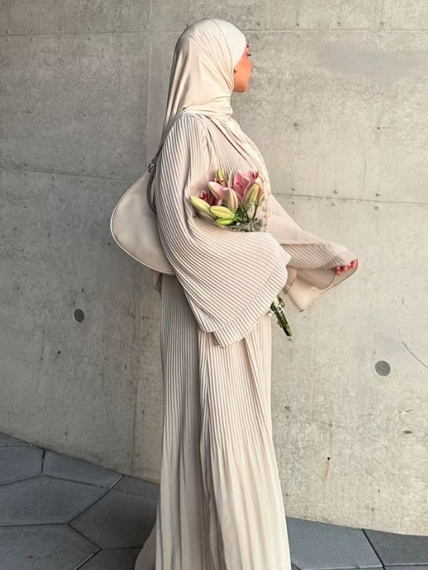 Vue de profil de l'abaya plissée Lys d'Ivoire en mouvement, montrant l'ampleur des manches évasées et le plissé vertical