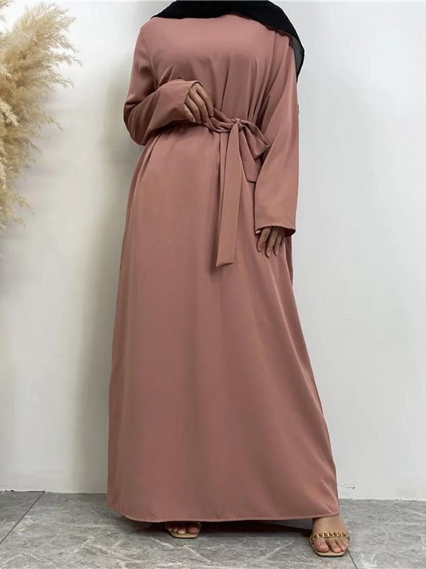 Une femme pose en abaya rose poudré ceinturée à la taille, avec un foulard noir