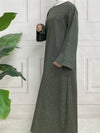 Une femme se tient de profil et porte une abaya en satin vert kaki