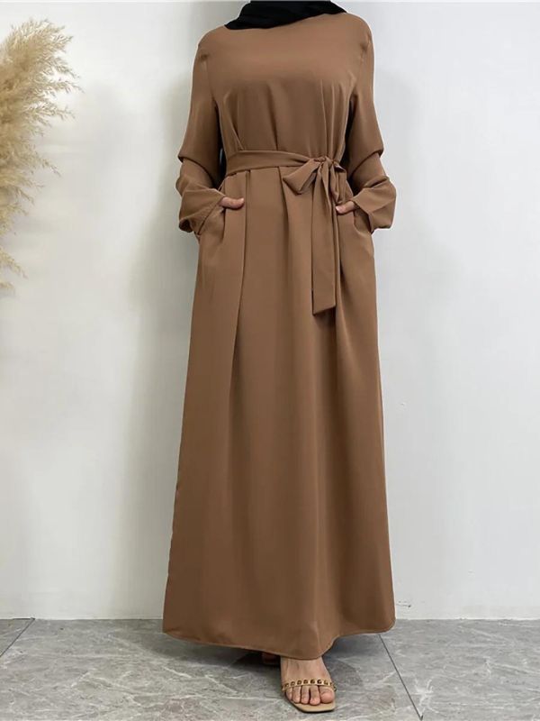 Une femme porte une abaya longue de couleur marron clair, fluide et ample, avec des manches longues et un hijab noir