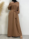 Femme portant une abaya longue et fluide de couleur marron clair, cintrée à la taille par une ceinture nouée assortie