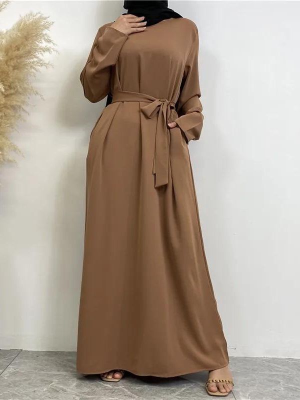 Femme portant une abaya longue et fluide de couleur marron clair, cintrée à la taille par une ceinture nouée assortie