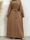 Une femme porte une abaya longue de couleur marron clair, ceinturée à la taille avec une ceinture assortie