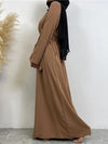 Vue latérale d&#39;une femme portant une abaya longue de couleur marron clair, ceinturée à la taille