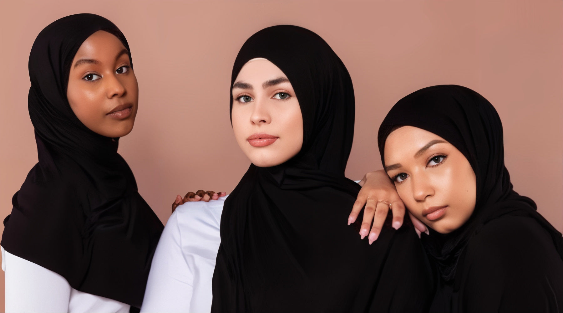 Trois femmes en hijabs noirs, posant ensemble. La première regarde à droite, la deuxième droit devant, et la troisième repose sa tête sur l’épaule de celle du centre