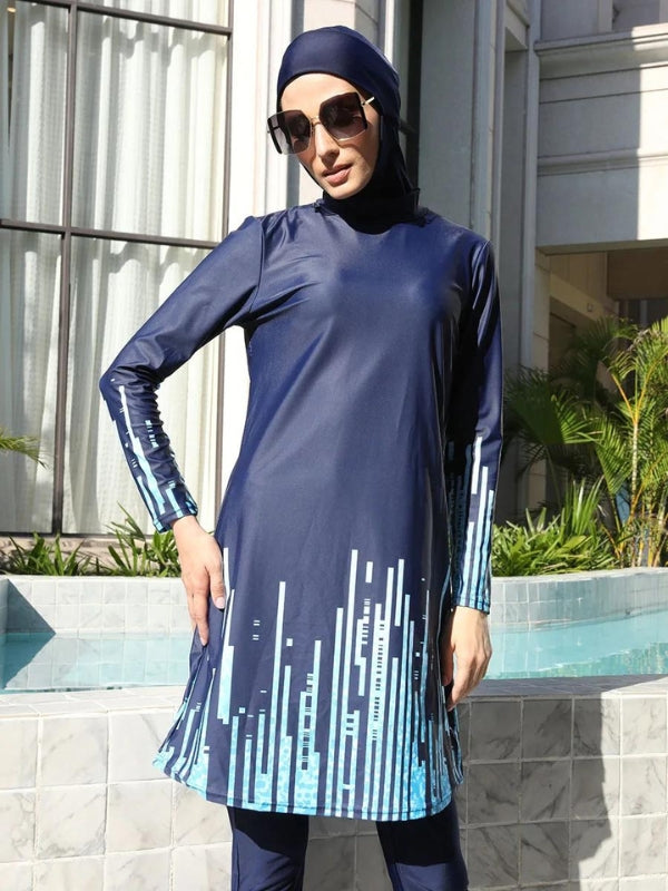 Une femme vêtue d'un burkini bleu marine avec des motifs géométriques bleu clair le long des manches et du bas de la tunique. Elle se tient près d'une piscine, portant des lunettes de soleil et regardant droit devant elle. Le design moderne du burkini, avec ses motifs verticaux stylisés, crée un contraste élégant avec le cadre environnant. Le décor de fond, composé d'un bâtiment classique et de végétation luxuriante, met en valeur l'ensemble tout en ajoutant une touche sophistiquée à la scène