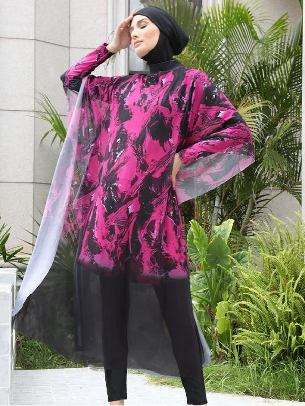 Une femme porte un burkini noir et rose avec des motifs abstraits éclatants. Une cape fluide et transparente assortie, flottant légèrement autour d'elle, ajoute une touche dramatique et élégante à sa tenue. La posture de la femme met en valeur le mouvement de la cape, créant un effet visuel de légèreté et de dynamisme dans un cadre urbain sophistiqué, entouré de verdure. L'ensemble offre un contraste saisissant entre les teintes sombres et vibrantes, soulignant à la fois l'élégance et la modernité