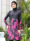 Une femme porte un burkini noir avec des motifs abstraits en rose vif qui s&#39;étendent sur toute la longueur de la tunique. Le voile noir assorti encadre son visage, ajoutant une touche d&#39;élégance à l&#39;ensemble. La tenue est mise en valeur par un cadre extérieur verdoyant, avec des plantes luxuriantes en arrière-plan, qui contraste joliment avec les couleurs vives du burkini