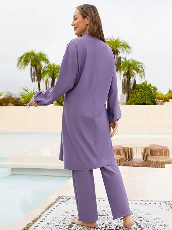 Femme de dos portant un burkini violet, posant avec grâce devant un décor de jardin