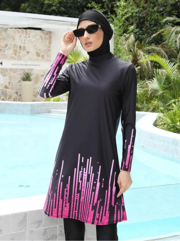 Une femme porte un burkini noir orné de motifs graphiques roses sur le bas de la tunique et les manches. La tenue est complétée par un hijab noir parfaitement assorti. Elle se tient debout près d'une piscine, dans un environnement verdoyant, affichant une allure à la fois élégante et moderne, alliant confort et style.