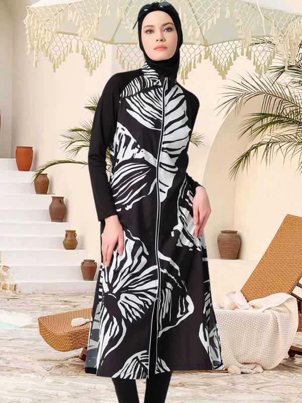 Burkini long noir à grandes feuilles blanches, vue de face dans un décor de terrasse, avec hijab et pantalon noirs
