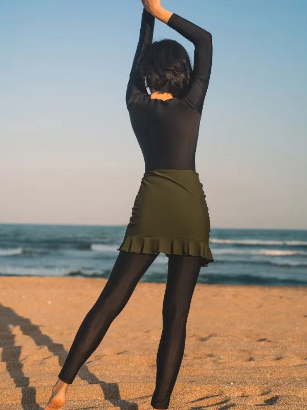 Vue arrière d&#39;une femme en burkini noir avec une jupe kaki bras levés face à l&#39;océan