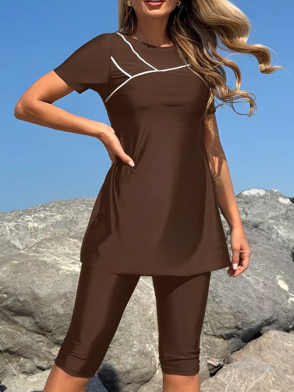 Burkini manche courte marron, tunique évasée à liséré blanc sur la poitrine, main sur la hanche, devant des rochers
