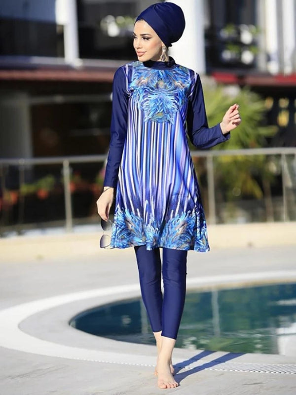 Une femme pose avec assurance dans une tenue de bain modeste élégante, composée d'une tunique bleu marine avec un motif de plumes bleues et des rayures verticales. La tunique, aux manches longues, est assortie à un legging bleu marine qui complète le look. Elle porte un turban assorti, ajoutant une touche de style supplémentaire à sa tenue