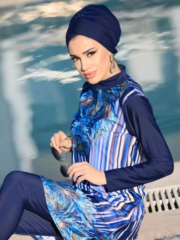 Une femme pose avec assurance dans une tenue de bain modeste élégante, composée d'une tunique bleu marine avec un motif de plumes bleues et des rayures verticales. La tunique, aux manches longues, est assortie à un legging bleu marine qui complète le look. Elle porte un turban assorti, ajoutant une touche de style supplémentaire à sa tenue