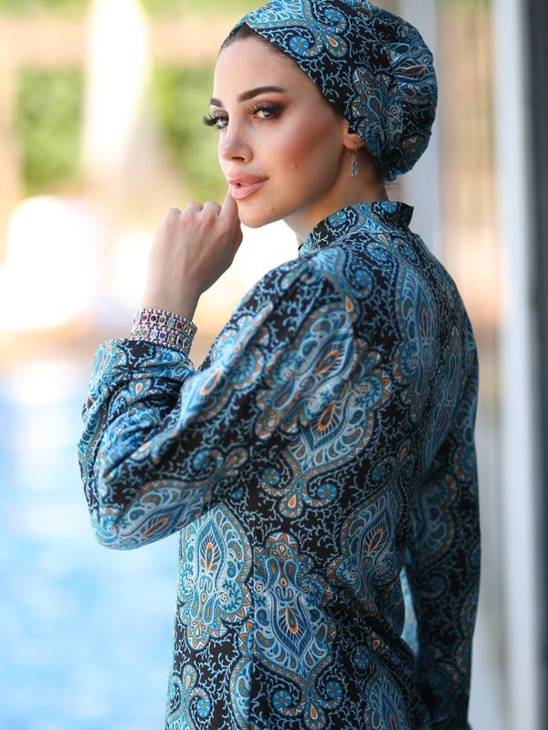 Une femme porte un burkini bleu océan et se tient de profil