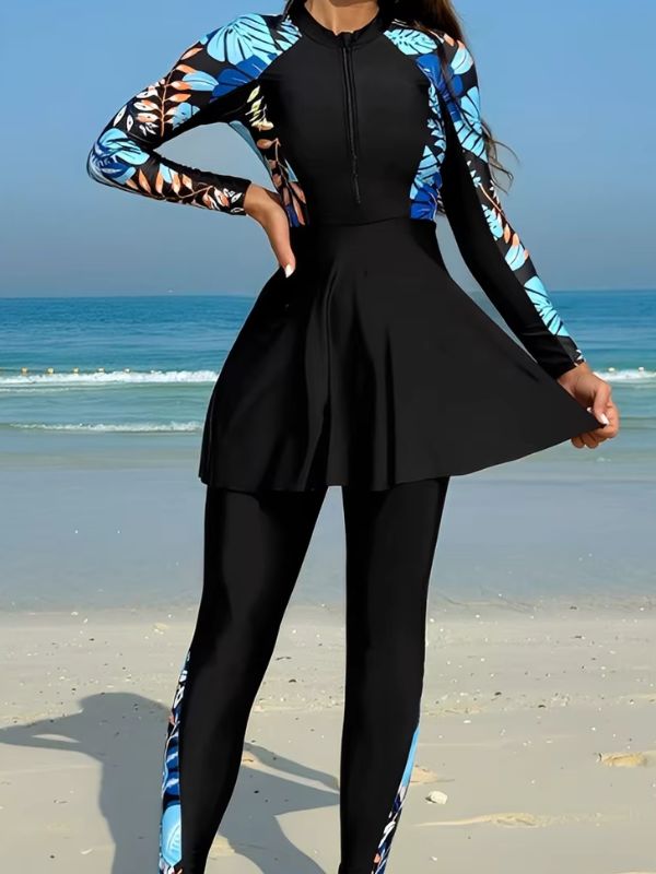 Burkini sport noir à feuillages bleus et orangés sur les manches, main sur la hanche, vue de face sur la plage