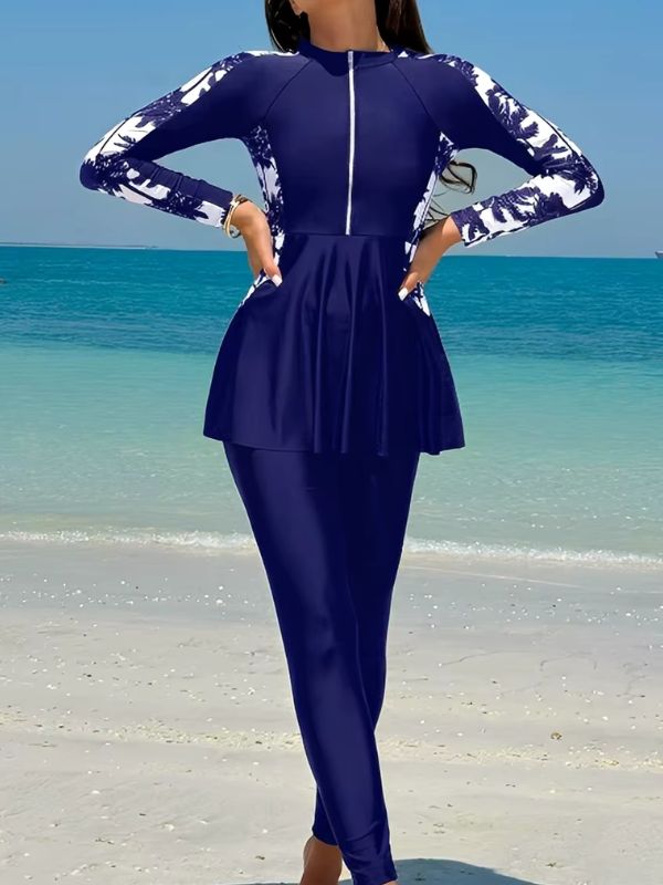 Burkini sport bleu marine à manches imprimées de palmiers blancs, vue de face, mains sur les hanches, au bord de l'eau
