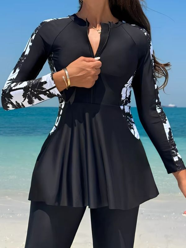 Burkini sport noir à manches ornées de palmiers noirs sur fond blanc, vue de face, mains sur les hanches, au bord de la mer