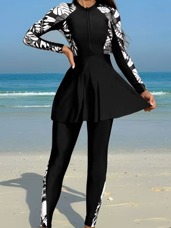 Burkini sport noir à feuillages noirs, gris et blancs, main sur la hanche, jupe évasée tenue à deux mains, vue de face