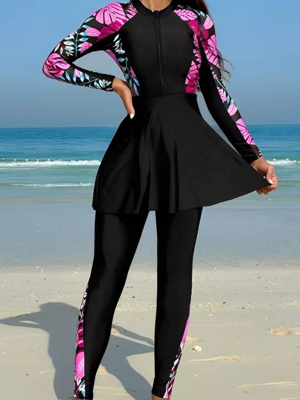 Burkini sport noir à feuillages roses et bleu ciel, main sur la hanche, jupe évasée tenue à deux mains, vue de face