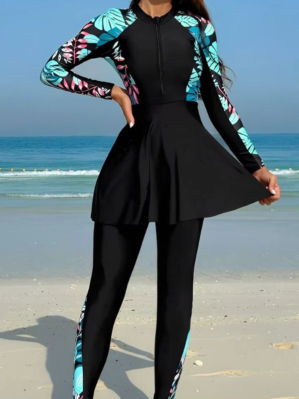 Burkini sport noir à feuillages turquoise et roses, main sur la hanche, jupe évasée tenue à deux mains, vue de face