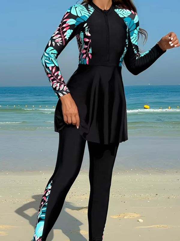 Burkini sport noir à feuillages turquoise et roses, en marche sur la plage, bande imprimée sur la jambe du pantalon