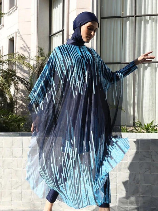 Une femme porte un burkini bleu marine orné de motifs géométriques bleus. La tenue est rehaussée par une cape transparente qui s'harmonise avec le burkini, flottant doucement autour d'elle. Le cadre élégant, avec des bâtiments modernes et une végétation verdoyante en arrière-plan, souligne l'allure à la fois sophistiquée et contemporaine de cette tenue. La femme est capturée dans un mouvement gracieux, ajoutant une touche de dynamisme à l'ensemble