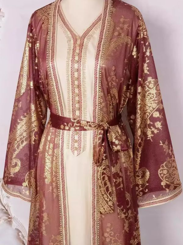 Un mannequin porte un caftan rose avec des motifs dorés, ceinturé à la taille