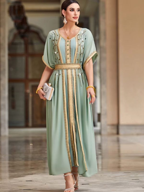 Femme portant un caftan marocain vert amande à manches papillon et galons dorés perlés, debout de face