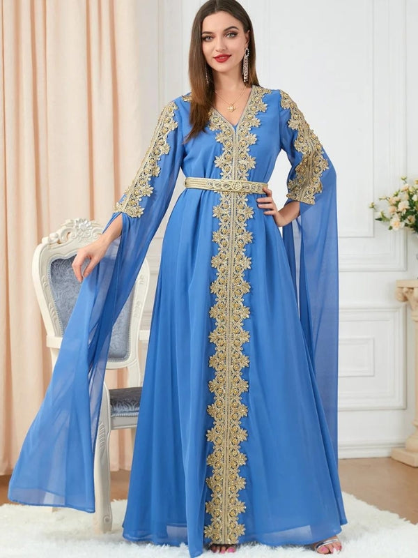 Femme vêtue d'un caftan bleu roi richement brodé de motifs dorés le long de l'encolure en V et descendant en ligne droite au centre de la robe. Les manches longues et amples ajoutent une touche de grâce au vêtement, qui est complété par une ceinture assortie soulignant la taille. Elle se tient debout dans une pièce élégante, posant avec confiance, et souriant légèrement. La scène est éclairée par une lumière douce, mettant en valeur les détails luxueux du caftan