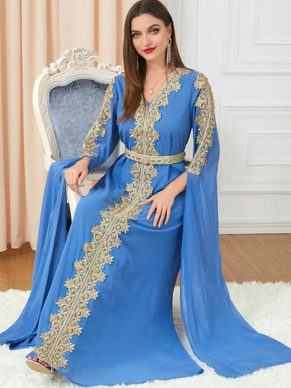 Femme vêtue d'un caftan bleu roi richement brodé de motifs dorés le long de l'encolure en V et descendant en ligne droite au centre de la robe. Les manches longues et amples ajoutent une touche de grâce au vêtement, qui est complété par une ceinture assortie soulignant la taille. Elle se tient debout dans une pièce élégante, posant avec confiance, et souriant légèrement. La scène est éclairée par une lumière douce, mettant en valeur les détails luxueux du caftan