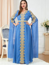 Femme debout, portant un magnifique caftan bleu roi orné de broderies dorées complexes le long de l&#39;ouverture frontale, des manches et autour du décolleté. Le caftan est cintré à la taille par une ceinture dorée assortie. Ses manches sont longues et amples, offrant une allure élégante et royale. La femme a les cheveux lisses, tombe sur ses épaules, et elle porte des boucles d&#39;oreilles longues et un collier délicat. Elle affiche un léger sourire, se tenant dans une posture gracieuse