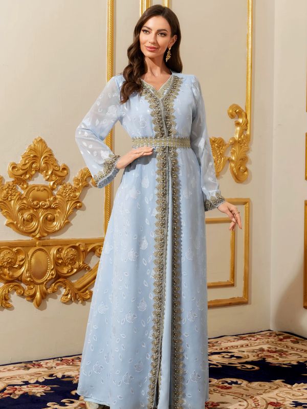 Femme portant un caftan marocain bleu ciel aux bordures dorées perlées, dans un décor raffiné