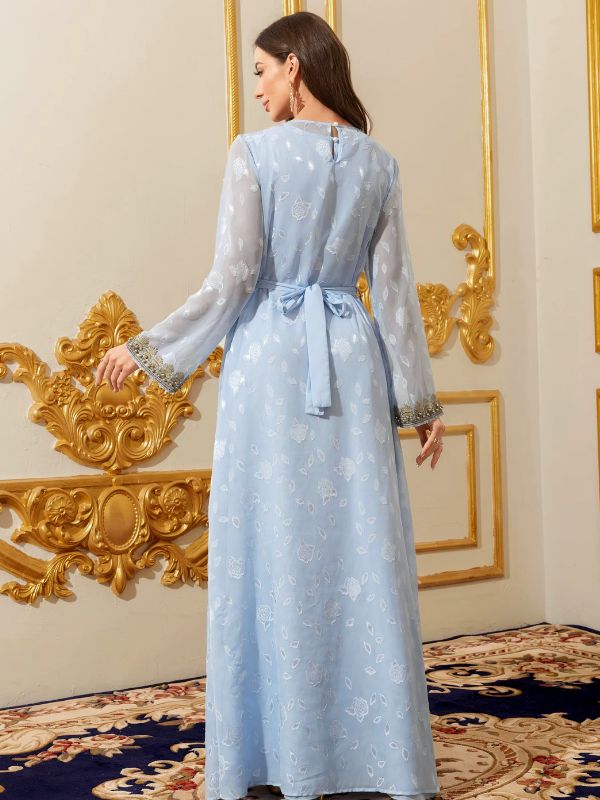 Femme portant un caftan marocain bleu ciel à motifs floraux, vue de dos, ceinture nouée et poignets ornés de perles dorées, dans un décor doré raffiné