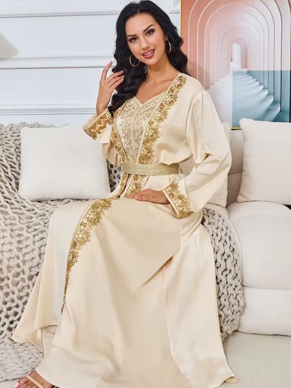 Une femme pose en caftan beige assise sur un canapé