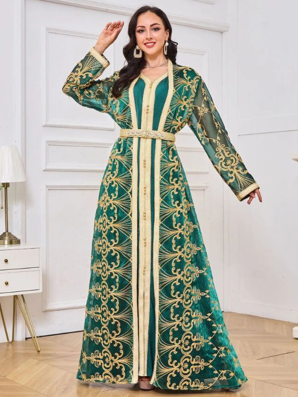 Une femme porte un caftan marocain vert émeraude élégant, confectionné dans un tissu satiné brillant et décoré de broderies fines