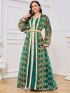 Une femme porte un caftan marocain vert émeraude aux motifs traditionnels brodés de fils dorés, descendant en cascade sur toute la tenue