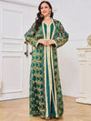 Une femme porte un caftan marocain vert émeraude avec une ceinture dorée ajustée à la taille, mettant en valeur sa silhouette