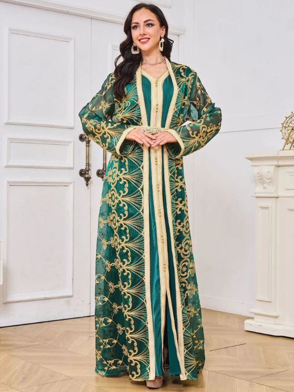 Une femme porte un caftan marocain vert émeraude élégant, confectionné dans un tissu satiné brillant et décoré de broderies fines