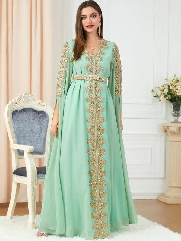 La femme est debout, face à la caméra, portant un élégant caftan vert menthe orné de broderies dorées. La ceinture dorée souligne délicatement sa taille, ajoutant une touche de raffinement à l'ensemble. Les détails de broderie sur les manches et le long du devant de la robe apportent une touche de sophistication et de luxe