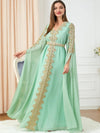 La femme est debout, vêtue d&#39;un magnifique caftan vert menthe, richement décoré de broderies dorées qui ornent le devant et les manches. Le caftan est cintré à la taille par une ceinture assortie, mettant en valeur sa silhouette. Les longues manches fluides ajoutent une touche d&#39;élégance et de grâce à l&#39;ensemble. Elle porte de longs cheveux lisses qui tombent librement sur ses épaules, et un maquillage subtil avec un rouge à lèvres rouge