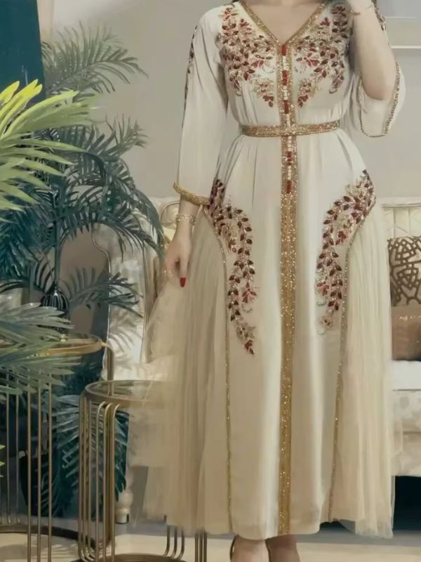 Femme portant un caftan marocain ivoire à broderies florales bordeaux et dorées serties de perles, col en V, jupon de tulle visible