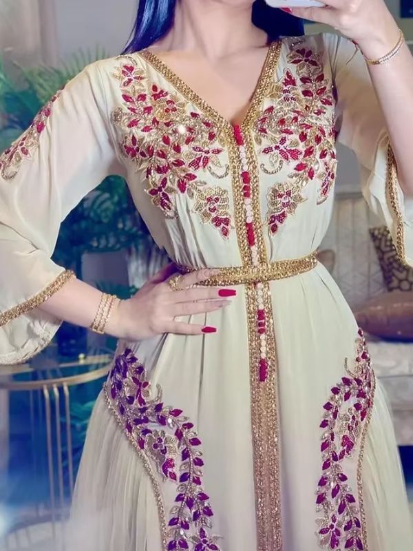 Femme portant un caftan marocain ivoire à broderies florales bordeaux et dorées serties de perles, col en V, jupon de tulle visible