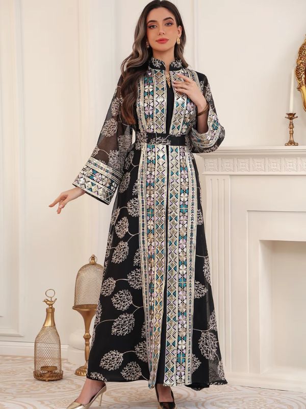 Femme en caftan noir brodé, porté ouvert sur une robe noire, orné de motifs géométriques dorés et turquoise.