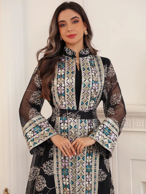 Vue rapprochée d'une femme en caftan noir à col montant, orné de broderies géométriques et florales pastel.